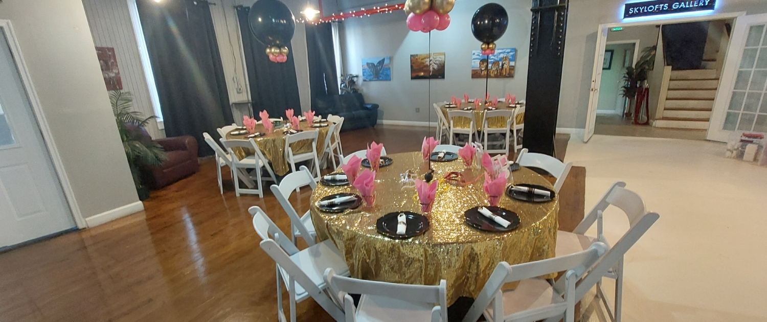 Round banquet table with gold sequin linen, pink napkins, and black-and-gold balloon centerpieces inside SkyLofts Gallery party venue set for a celebration event.