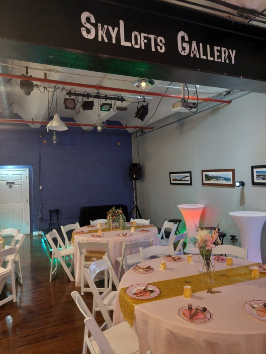 Intimate bridal-shower setup with pink linens, floral centerpieces, and lounge tables inside SkyLofts Gallery event space.
