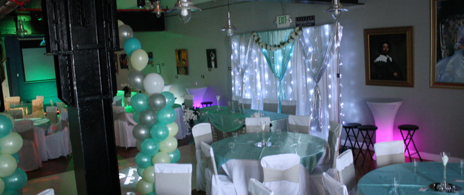 Teal-and-white balloon columns and twinkle-light drapery backdrop decorating SkyLofts Gallery event space for an elegant celebration.