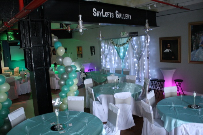 Teal-and-white balloon columns and twinkle-light drapery backdrop decorating SkyLofts Gallery event space for an elegant celebration.