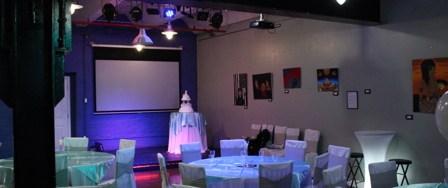 Reception setup at SkyLofts Gallery featuring teal-draped tables, white chair covers, and a cake table beneath a projector screen—perfect for weddings and other events.